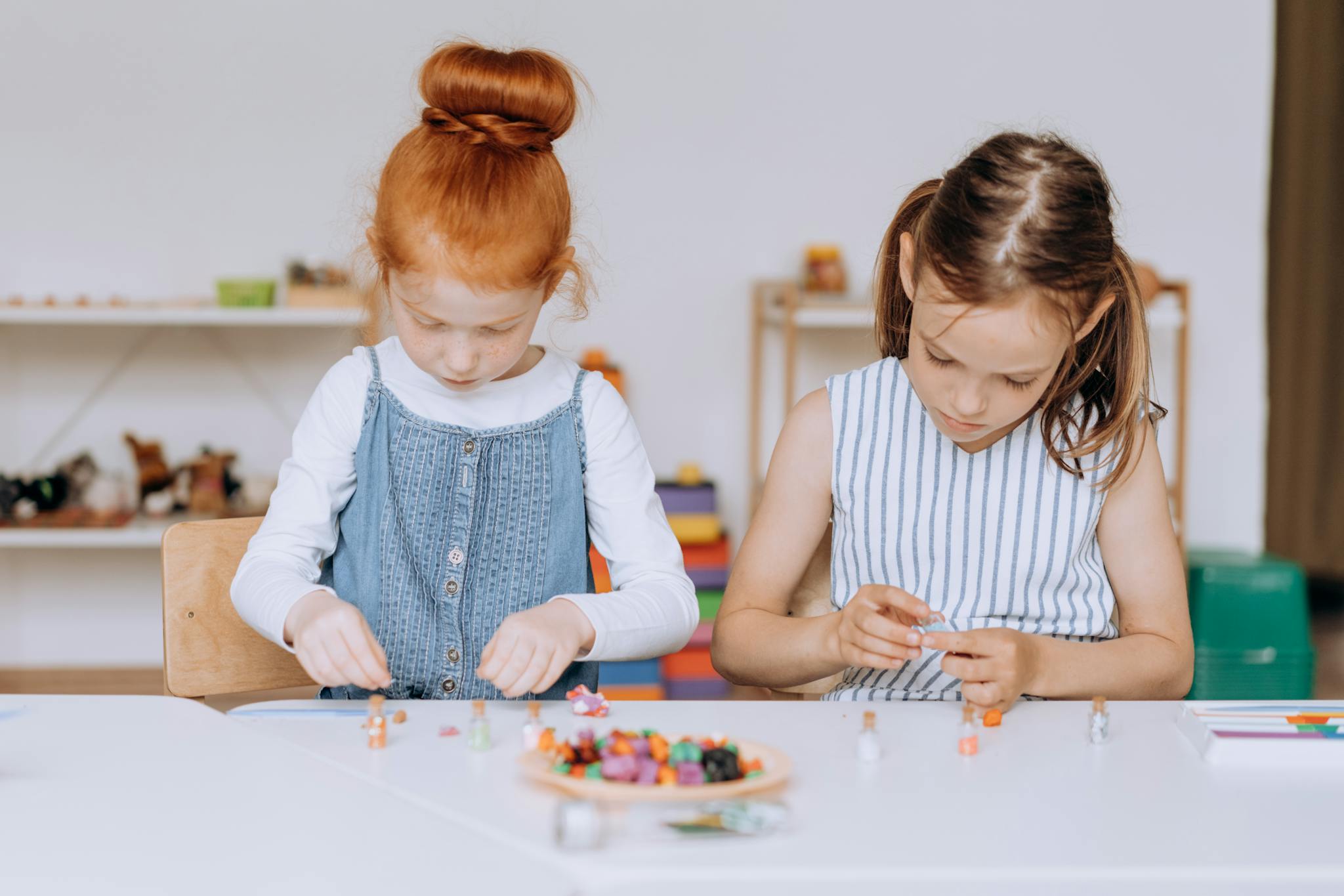 Más servicios Two young girls actively engaged in a creative project at a classroom table, fostering education and creativity.